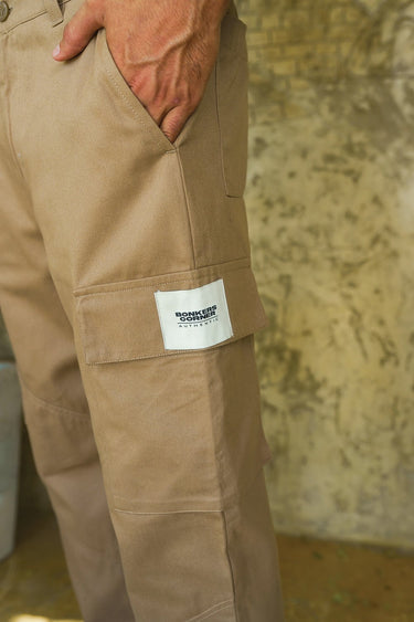 Beige cargo pants with utility pockets by Bonkers Corner, featuring multiple functional pockets and a relaxed fit.