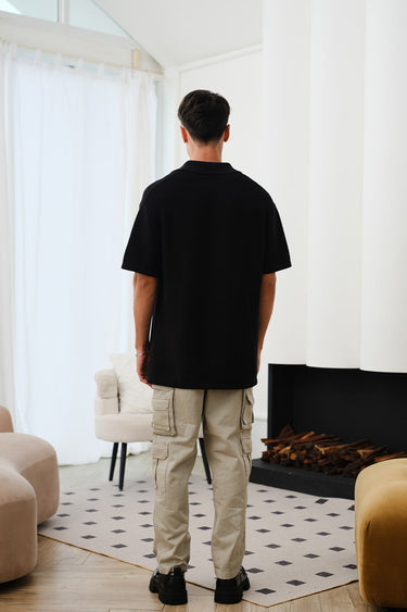Black knit textured polo T-shirt from Bonkers Corner, featuring a classic collar and short sleeves, styled for casual wear.