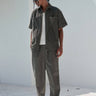 Bonkers Corner olive corduroy pants, slim-fit style with textured fabric, shown on a model with pockets and waistband detail.