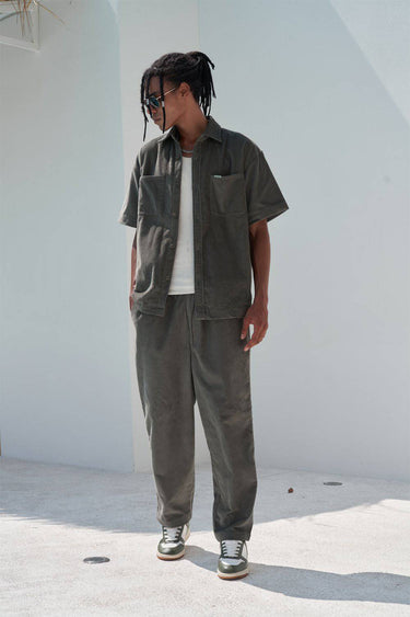 Bonkers Corner olive corduroy pants, slim-fit style with textured fabric, shown on a model with pockets and waistband detail.