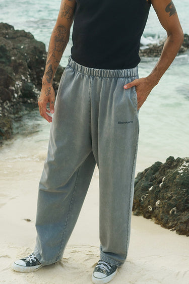 Man wearing grey loose fit pants styled with a minimal top in a beachside setting. A relaxed example of men’s Valentine’s Day outfit ideas, showcasing a comfortable yet stylish Valentine’s Day outfit men can wear for a casual dinner date look.